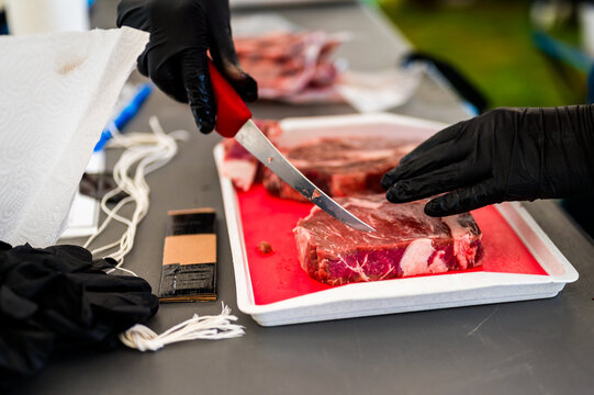 Close up of a chef precisely trimming a thick cut ribeye steak with a sharp knife on a cutting board during a professional Steak Cookoff Association SCA BBQ competition
