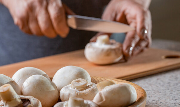 Mushrooms on wooden table. Chef cutting, slicing mushrooms champignon closeup. Hands cooking healthy vegetables