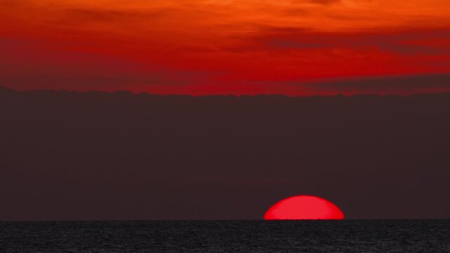 Dramatic red sunset above the sea horizon near Phuket, Thailand with glowing sun and dark silhouettes.