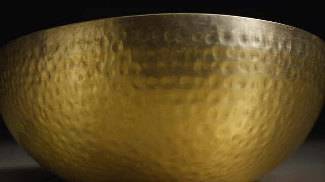 Hammered golden bowl with textured surface displayed from various angles, showcasing its reflective qualities and intricate craftsmanship in a dark setting