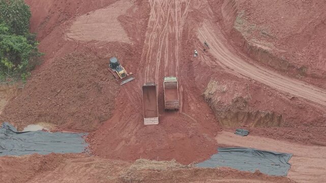 A crawler bulldozer is leveling the fill soil unloaded from a truck for road construction