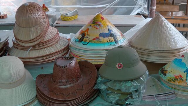 Vietnamese bamboo non la conical hats with colorful drawings and plain ones, Vietnamese People's Army pith coi helmets and cowboy hats are sold as souvenirs at the street vendors shop
