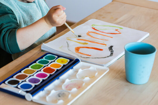 Toddler painting with watercolors and brush, close-up, hand only