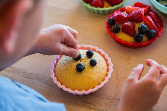 Children decorating a homemade cake with berries, close-up