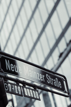 Behind the Neue Mainzer Strasse sign, Frankfurt glass facade reflection and blur create a vertical street frame within financial architecture