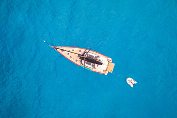 Fototapeta premium High-angle aerial drone shot of a red and white sailboat anchored in crystal-clear turquoise ocean water. A serene image capturing the essence of a luxury summer sailing holiday and tropical adventure