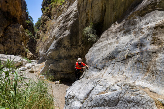 Female hiker using a fixed rope to navigate a steep rock wall in Sarakina Gorge