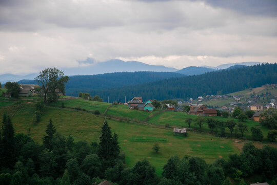 Picturesque mountain landscape. Ukrainian Carpathians. A cozy village lies in the valley below, surrounded by rolling green hills and misty mountain peaks. Bright traditional houses and untouched