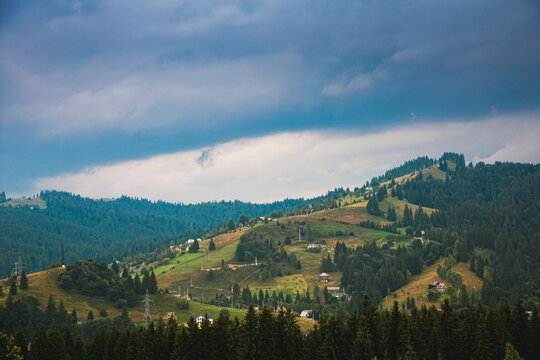 Picturesque mountain landscape. Ukrainian Carpathians. A cozy village lies in the valley below, surrounded by rolling green hills and misty mountain peaks. Bright traditional houses and untouched