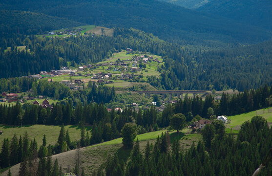 Picturesque mountain landscape. Ukrainian Carpathians. A cozy village lies in the valley below, surrounded by rolling green hills and misty mountain peaks. Bright traditional houses and untouched