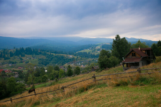 Picturesque mountain landscape. Ukrainian Carpathians. A cozy village lies in the valley below, surrounded by rolling green hills and misty mountain peaks. Bright traditional houses and untouched