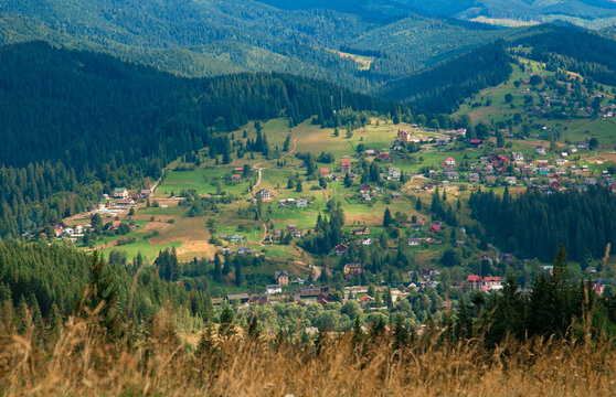 Picturesque mountain landscape. Ukrainian Carpathians. A cozy village lies in the valley below, surrounded by rolling green hills and misty mountain peaks. Bright traditional houses and untouched