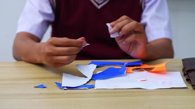 Student tearing colorful paper scraps at wooden desk for creative collage or art project