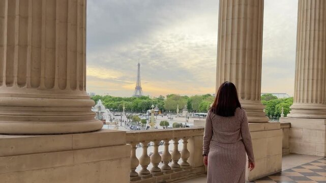 Stylish brunette woman walking toward a balcony overlooking the beautiful Eiffel Tower in Paris, France, enjoying her european vacation and sightseeing