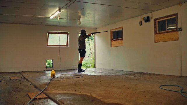 A Person is Cleaning an Empty Indoor Room Using a Pressure Washer - Static Shot