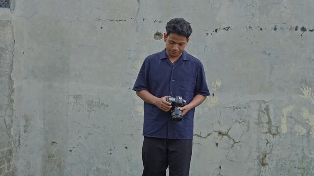 Asian journalist holding professional camera looking around and wiping sweat during outdoor shoot