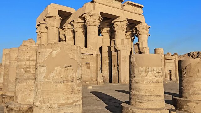 Kom Ombo temple ruins with double columns and composite capitals against clear blue sky in Egypt, ancient Ptolemaic architecture dedicated to Sobek and Horus with damaged walls.