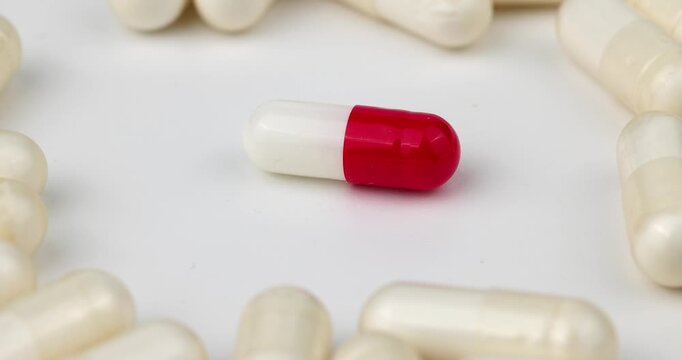 Medical stock video showing a central bi-color pill rotating inside a circle of plain white tablets. Perfect for pharmaceutical media design projects.