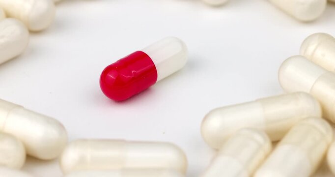 Spinning bi-color capsule pill surrounded by multiple white pills rotating in a clear circle for clinical and healthcare concepts.