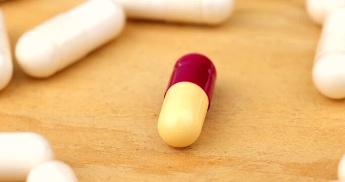 Unique bi-color capsule spinning in a moving circle of white drug pills rotating together for pharmacy and science video concepts.