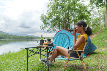 Fototapeta premium Black woman taking photos with camera while camping by lake in nature