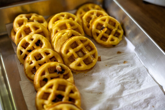 Delicious golden brown baked mini waffles arranged on white paper inside metal baking tray waiting to be served for delightful breakfast or sweet snack