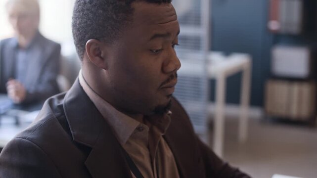 Tilt up handheld shot of Black male adult developer typing on keyboard of laptop while working at desk in modern office
