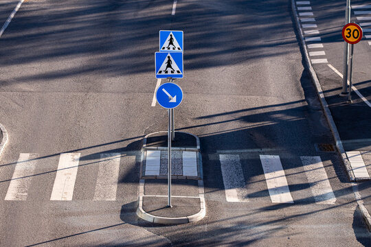 long shadow patterns stretch over a crosswalk and pedestrian sign on an island, shaping asphalt road marking across a quiet street curve