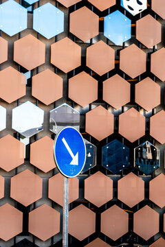 a geometric hexagon pattern covers a reflective facade as an arrow sign cuts upward, turning the building surface into urban texture