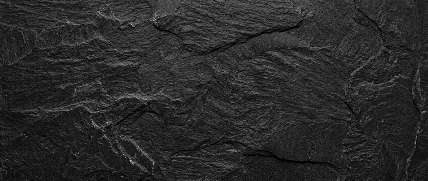 A rough-textured natural slate surface in deep gray and black tones. A natural stone texture with a rustic yet modern look, ideal as a backdrop for design projects.