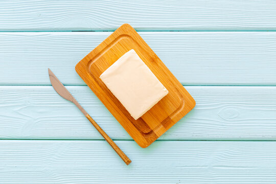 Block of fresh butter in wooden butter dish and a knife, top view