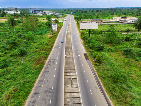 Aerial view of a multi-lane highway stretching through lush tropical vegetation with billboards and distant buildings under an overcast sky in Port Harcourt, Rivers, Nigeria.