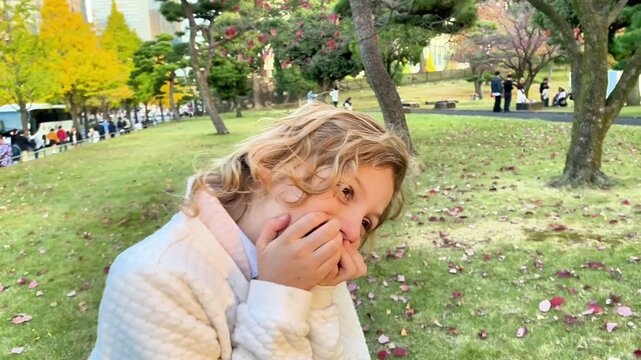  Young blonde girl giggling and covering her mouth in an autumn park