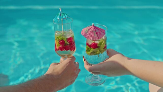 Couple toasting with refreshing summer cocktails by poolside in slow motion.