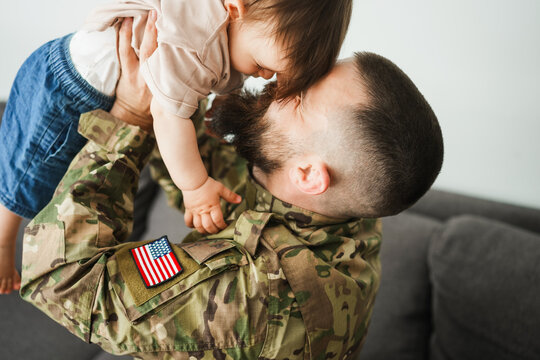 Male american soldier in military uniform hugs his little son at home - Emotional father happy homecoming concept - Main focus on toddler face