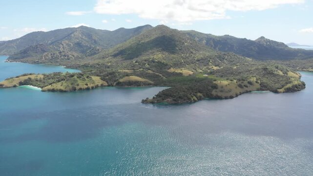 Aerial panorama of Pulau Rinca Komodo in Flores, Indonesia, featuring lush green hills surrounded by deep blue tropical waters under bright clouds and clear daylight skies
