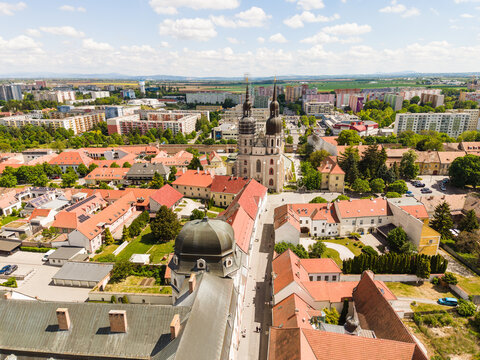 Aerial view of the historic St. Nicholas Basilica with its twin towers surrounded by red-tiled rooftops and lush greenery in Trnava, Trnava Region, Slovakia.