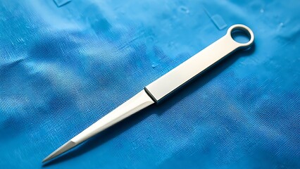 Naklejka premium A single surgical scalpel resting on a sterile blue cloth, sharp blade in focus.