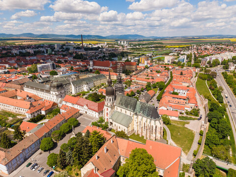 Aerial view of St. Nicholas Basilica surrounded by historic red-roofed buildings, lush green trees, and the old city walls in Trnava, Trnava Region, Slovakia.