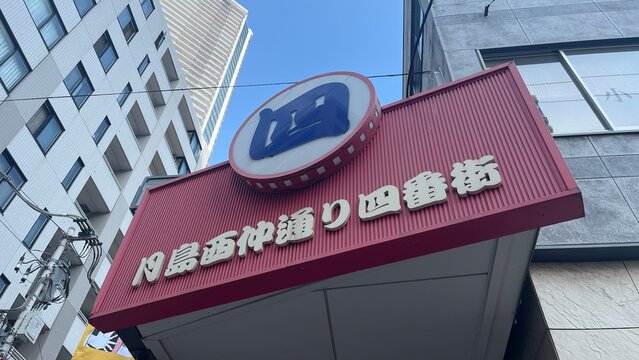 Monja Street entrance sign for Tsukishima Nishinakadori Fourth Street in the Chuo district featuring iconic red cladding and blue logo - Tokyo, Japan, October 17, 2025