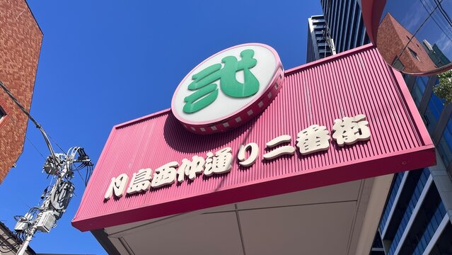 Monja Maruta 2-bangai restaurant signage and pink awning entrance located in Tsukishima Monja Street area against a clear blue sky - Tokyo, Japan, October 17, 2025