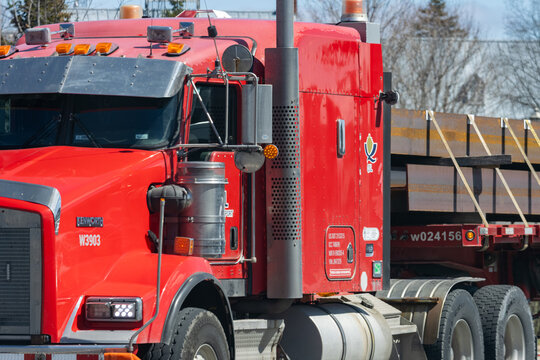 Quebec, Canada, 24 April 2026 : A red Kenworth semi truck hauls steel plates on a flatbed trailer.