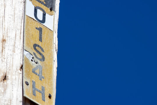 Quebec, Canada, 26 April 2026 : A weathered wooden pole features a yellow and white identification marker with black alphanumeric characters against a blue sky.
