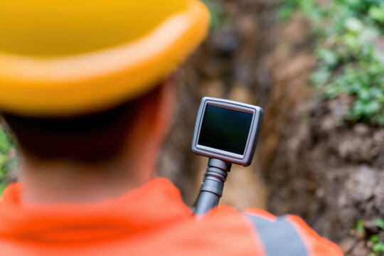 Sewer maintenance technician inspecting residential drain line with camera in outdoor trench