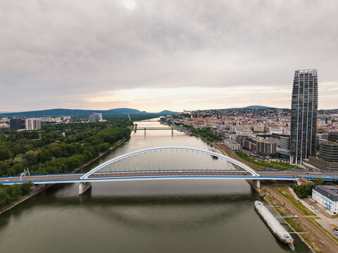 Aerial view of the Apollo Bridge over the Danube river with the city skyline and Eurovea Tower under a cloudy sky in Bratislava, Bratislava Region, Slovakia.
