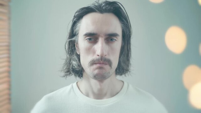 Loneliness comical mustache Close-up of calm man with medium dark hair and mustache wearing white shirt looking directly at camera with slight eye movements soft warm lighting and blurred background
