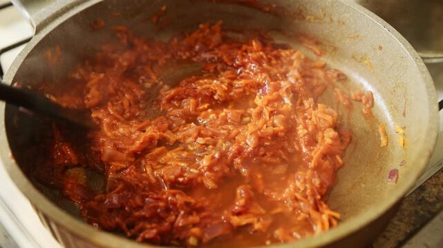 Stirring tomato paste with onions and grated carrots in frying pan cooking process close up