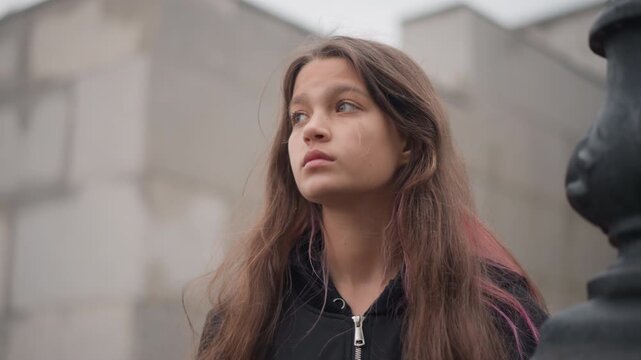 Girl pauses beside rainfilled puddles quietly. Young woman stands near wall with wet hair contemplative mood. Female figure pauses alone by rainy sidewalk in reflective and somber state of mind
