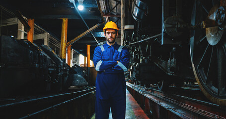Worker stands with arms crossed, wearing blue overalls and a yellow helmet © lovelyday12