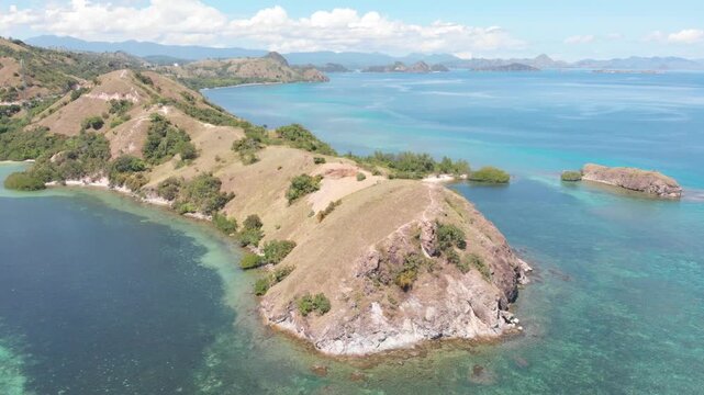 Aerial view of the northern headland near Labuan Bajo in Komodo National Park, Indonesia, surrounded by vibrant coral reefs and turquoise tropical waters under a sunny blue sky